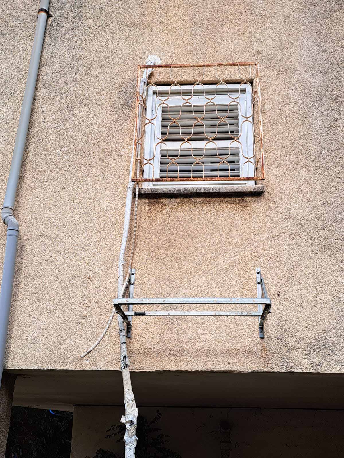 תושבת מזגן מיותמת על הקיר החיצוני של הבניין, לאחר שהמזגן נגנב, והכבלים של המזגן תלויים ליד התושבת.