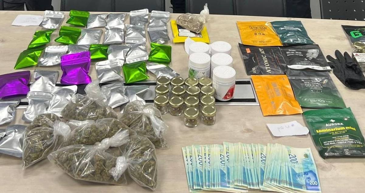 סמים שנתפסו במחסום בהרצליה. על שולחן מונחות שקיות שקופות ושקיות צבעוניות עם חומר חשוד. לידן מונחים שטרות של 200 שקלים, כפפות, טלפונים סלולריים, מפתחות וקופסאות עם חומרים.