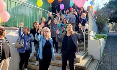 קבלת פנים לסבתא של לירי אלבג. חבורה גדולה של נשים עומדות עם בלונים צבעוניים בפתח של בניין על גרם המדרגות.