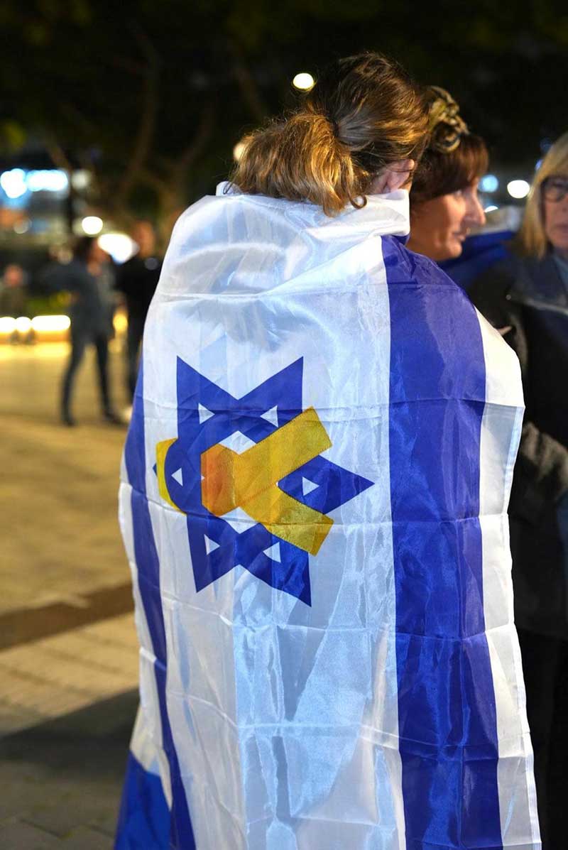 אישה עטופה בדגל ישראל עם סמל החטופים משולב במגן דוד. התכנסות תושבי העיר רעננה לכבוד שחרורה של נעמה לוי