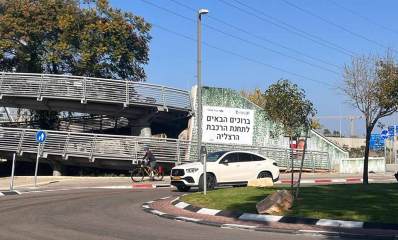 תחנת הרכבת הרצליה. בצד ימין כיכר ומכונית לבנה. ברקע גשרים להולכי רגל, ועל העלייה לגשרים שלט גדול עם כיתוב: ברוכים הבאים לתחנת הרכבת הרצליה.