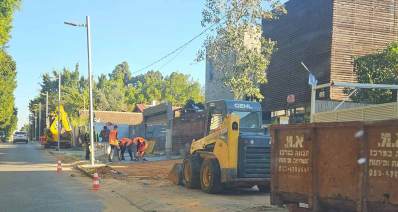 עבודות פיתוח ברחוב כצנלסון בכפר סבא. על המדרכה חונה טרקטור ולידו מיכל גדול לאיסוף פסולת הנייה. שלושה פועלים מרצפים את המדרכה.