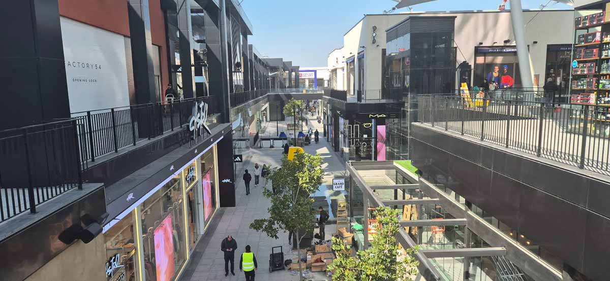 ביג פאשן גלילות. צילום מקומה שנייה ושתי הקומות בתמונה. חנויות בצד ימין ובצד שמאל וביניהן נראית קומה ראשונה שבמרכזה צמחייה, ספסלים, ואנשים..