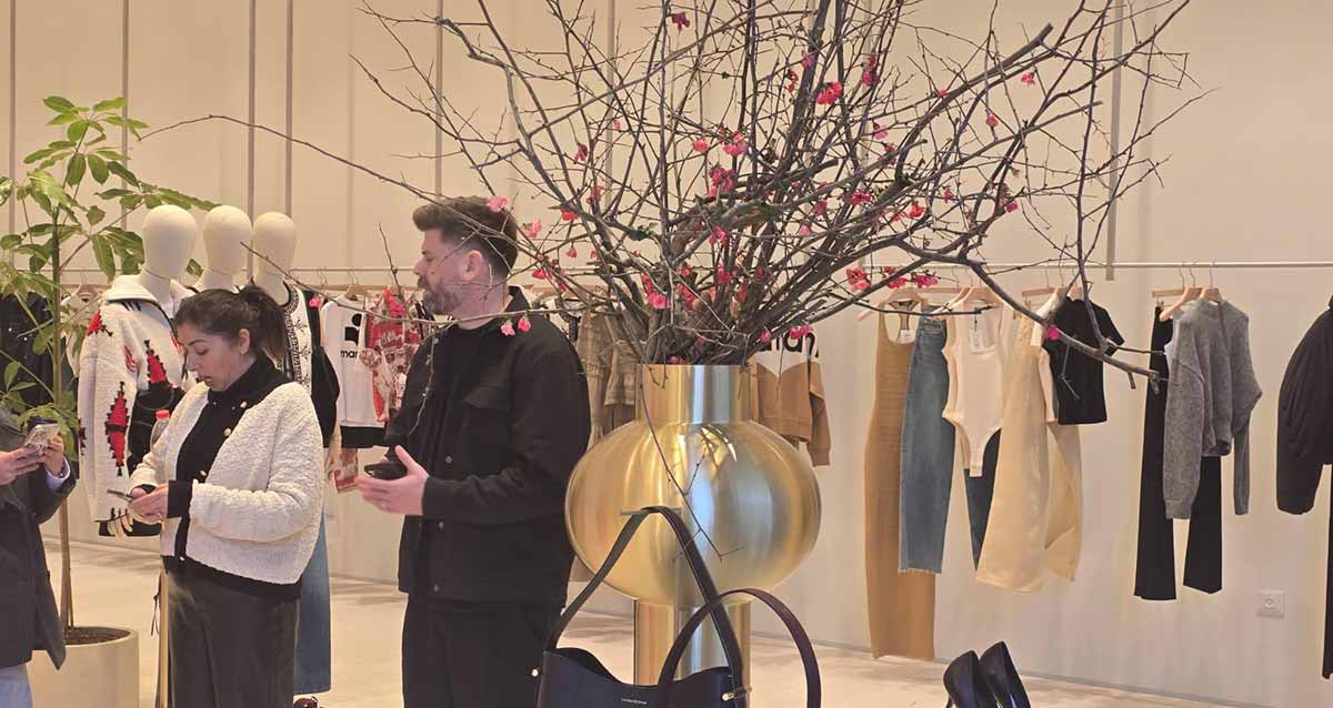 ביג פאשן גלילות - הכנות אחרונות לפתיחה. תמונה של חנות בגדים התלויים על מתלה בחנות. שני אנשים עם טלפונים ביד בתוך החנות.