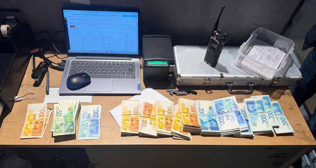 קזינו לא חוקי בהרצליה פיתוח. על שולחן מונחים שטרי כסף של 200, 100, 50 שקלים. מחשב נייד ומדפסת. מזוודה מאלומיניום.