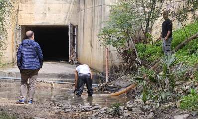 ניקוי שלולית הסולר בנחל גלילות - בין שכונת נווה ישראל לשכונת גליל ים. השלולית בפתח של מעביר מים גדול עם שערים. צינור ניקוז יורד לשלולית בה עומד עובד עם בגד גומי. שני אנשים עומדים מחוץ לשלולית.