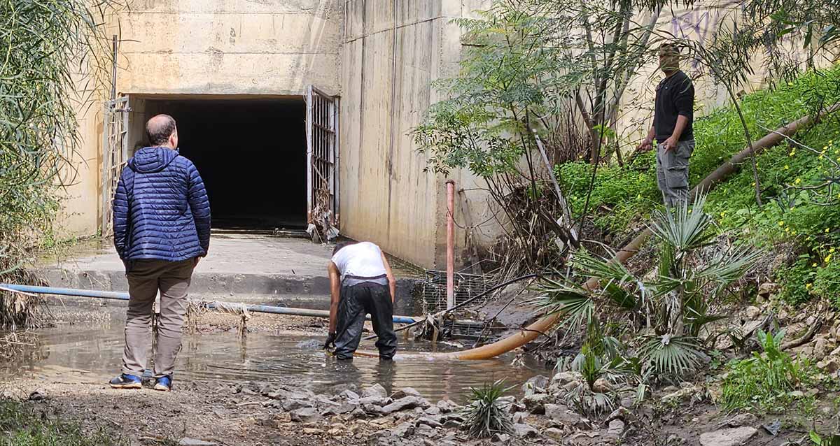 ניקוי שלולית הסולר בנחל גלילות - בין שכונת נווה ישראל לשכונת גליל ים. השלולית בפתח של מעביר מים גדול עם שערים. צינור ניקוז יורד לשלולית בה עומד עובד עם בגד גומי. שני אנשים עומדים מחוץ לשלולית.