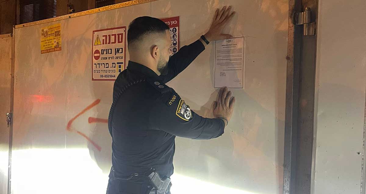 שוטר מדביק צו סגירה זמנית על גדר של אתר בנייה בכפר סבא עקב תפיסת עובדים שוהים בלתי חוקיים