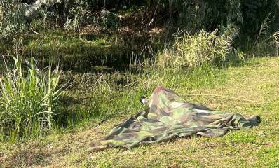 צלם ציפורים מוסווה מצלם עם עדשה גדולה עופות מים בפארק. הצלם שוכב על הדשא מכוסה ביריעת הסוואה.