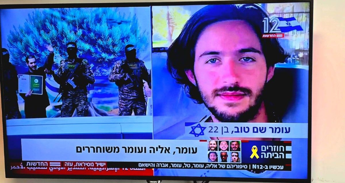 עומר שם טוב, מימין, על הבמה בעזה - מחויך ומנופף בידיו. צילום מסך מתוך ערוץ 12