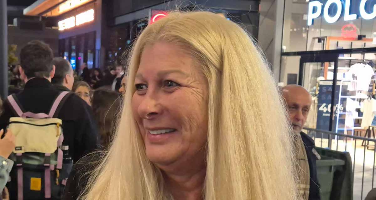 אורלי בר. תמונה של הפנים, עם שיער בלונדיני, על רקע חנות של POLO. מאחוריה אנשים.