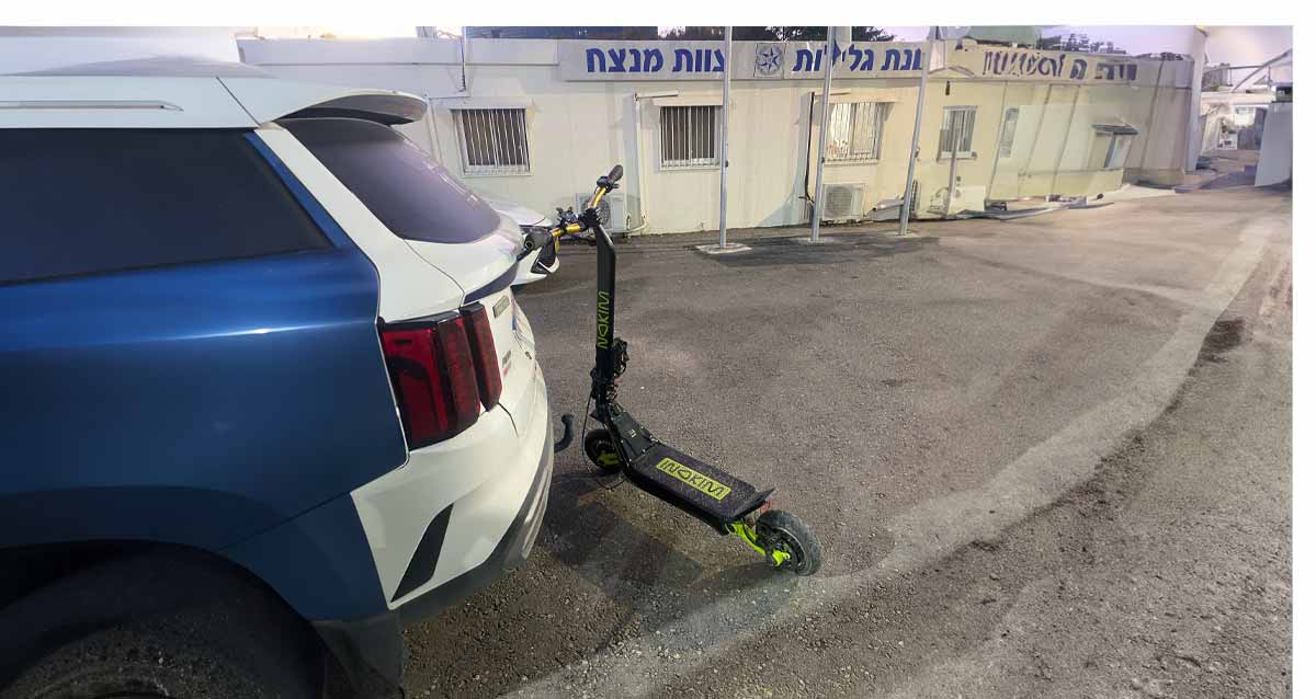 הקורקינט בתחנת גלילות נשען על מכונית משטרה. ברקע בניין המשטרה עם הכיתוב: תחנת גלילות צוות מנצח