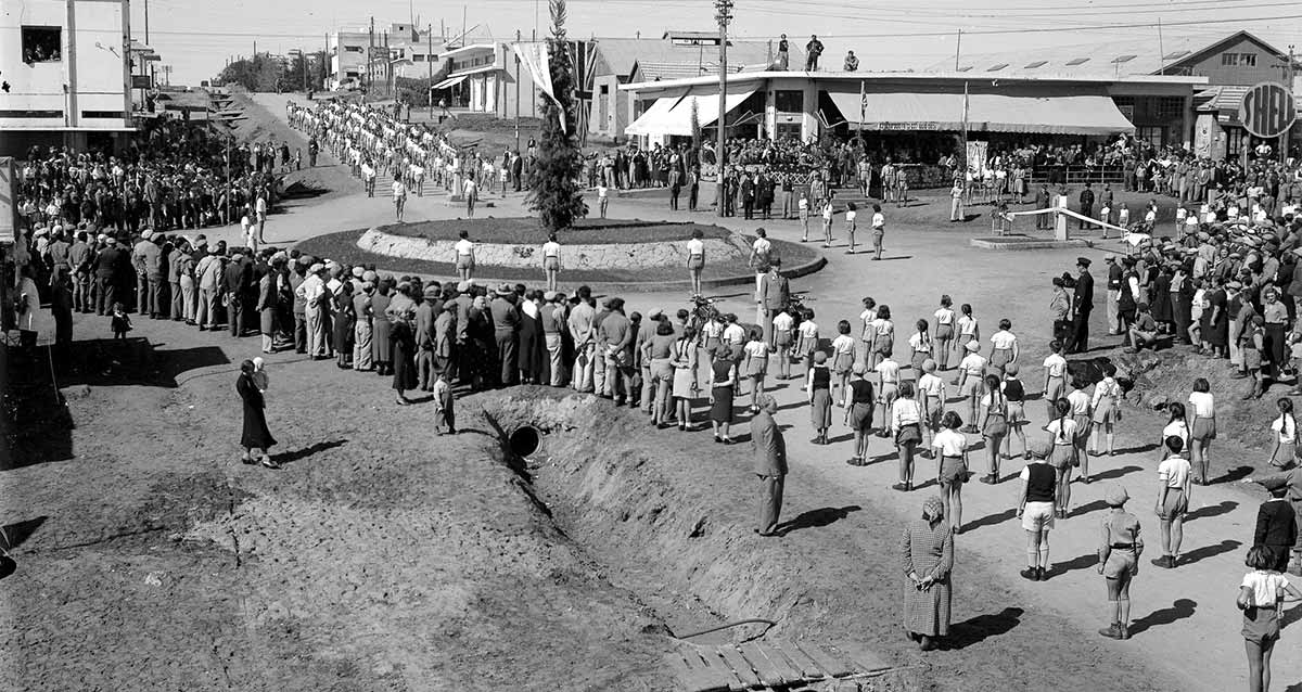 טקס חנוכת שני הרחובות הפנימיים הסלולים הראשונים בכפר סבא. במרכז התמונה כיכר עם דשא ועץ במרכזה. בארבעה רחובות המגיעים לכיכר עומדים תלמידים בשורות באמצע הרחובות ובשולי הרחובות קהל רב.