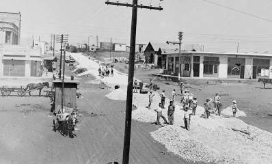 סלילת רחוב השרון - לימים רחוב ויצמן בכפר סבא. עובדים מפזרים חצץ לאורך הרחוב. מימין ומשמאל עגלות משא עם סוסים.