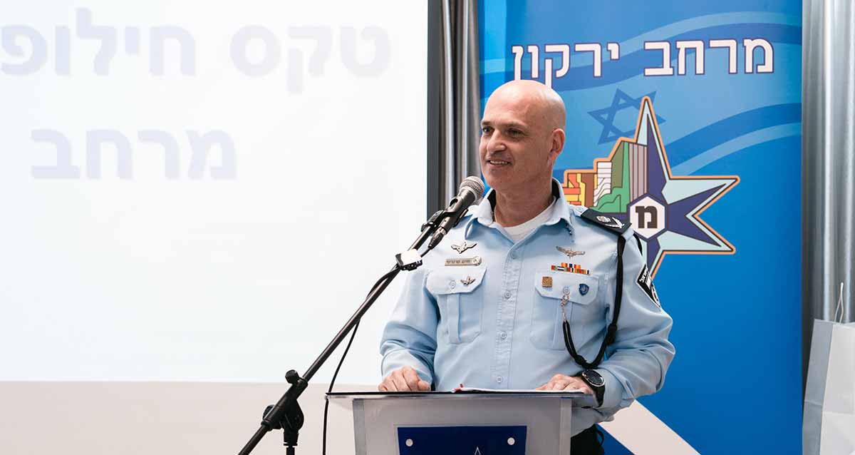 ניצב חיים סרגרוף מפקד מחוז ת"א. עומד לפני דוכן נואמים עם מיקרופון לפניו. מאחוריו סמל המשטרה והכיתוב: מרחב ירקון