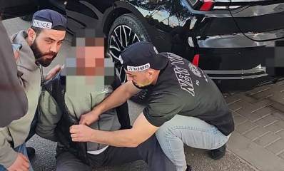 החשוד בדקירה בתחנת הדלק בגלילות. שני שוטרים עושים חיפוש על החשוד היושב על המדרכה.