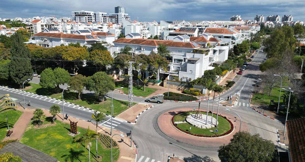 שדרוג שכונת 2004 ברעננה. צילום מגבוה של השכונה בהצטלבות של שני רחובות. כיכר עגולה עם ירק ועמוגדים בהצטלבות הרחובות. השכונה של בתים בני 4 קומות עם גגות רעפים. ברקע בניינים גבוהים. רחוב אחד הוא עם שני מסלולים ושדרה באמצע.