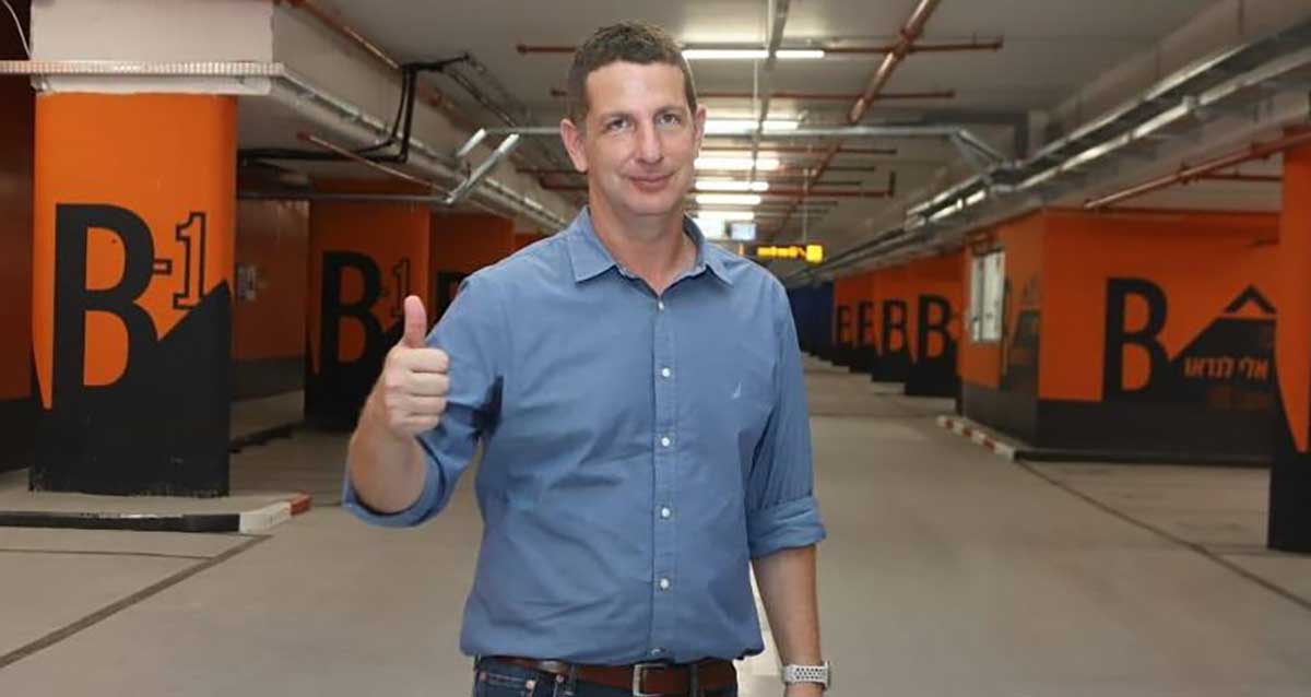 יריב פישר בחניון תת קרקעי, מרים אגודל. חניון B -1 עם הכתובת אלי לנדאו על הקירות והעמודים