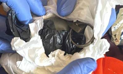 רימון רסס בדירה ברמת השרון עטוף בפלסטיק שחור ובניירות, ואצבעות השוטרים עם כפפות כחולות חושפות את הרימון.