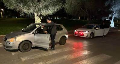 תפיסת סמים ברמת השרון. שוטר עומד ליד רכב אפור שדלת הנהג פתוחה. הרכב עומד על מעבר חצייה. מאחורי הרכב חונה רכב נוסף בצבע לבן ואורות דולקים.