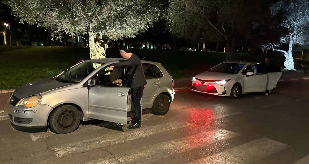 תפיסת סמים ברמת השרון. שוטר עומד ליד רכב אפור שדלת הנהג פתוחה. הרכב עומד על מעבר חצייה. מאחורי הרכב חונה רכב נוסף בצבע לבן ואורות דולקים.