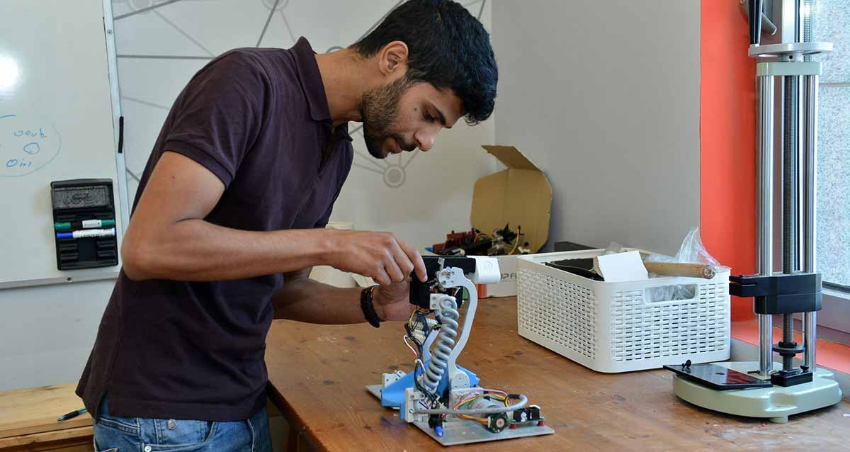 צוות גיאומטריקס רעננה. עובד החברה עומד ליד שולחן עבודה ומטפל במכשיר. על השולחן קופסה ומכשיר ארוך.