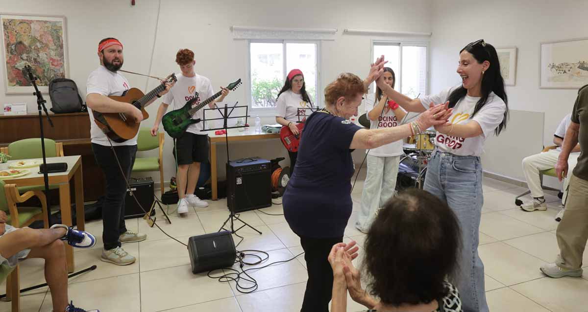"יום מעשים טובים" בהרצליה. שלושה נגני גיטרה מנגנים ובאולם בחורה צעירה רוקדת עם אישה מבוגרת.