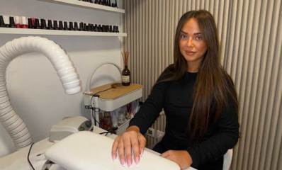 נטלי טל הזז, במכון ציפורניים, יד ימין על משטח הטיפול. מעליו צינור לייבוש, ועל הקיר בקבוקונים לציפורניים.