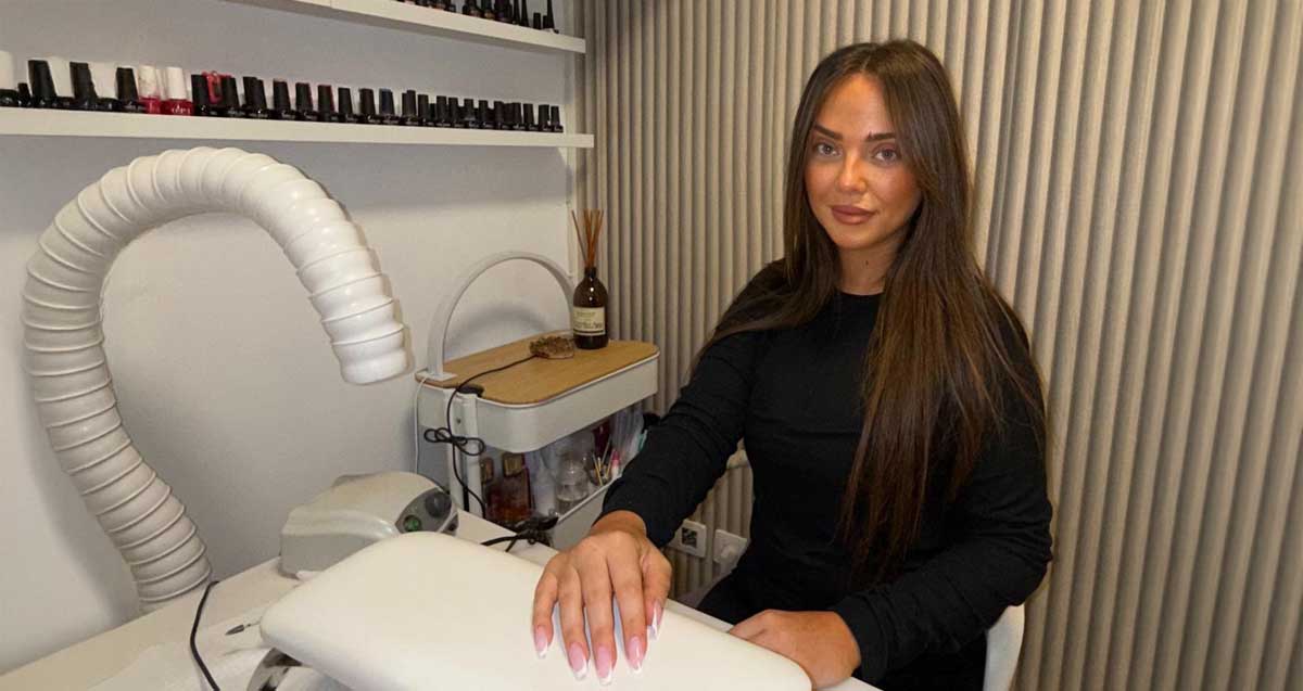 נטלי טל הזז, במכון ציפורניים, יד ימין על משטח הטיפול. מעליו צינור לייבוש, ועל הקיר בקבוקונים לציפורניים.