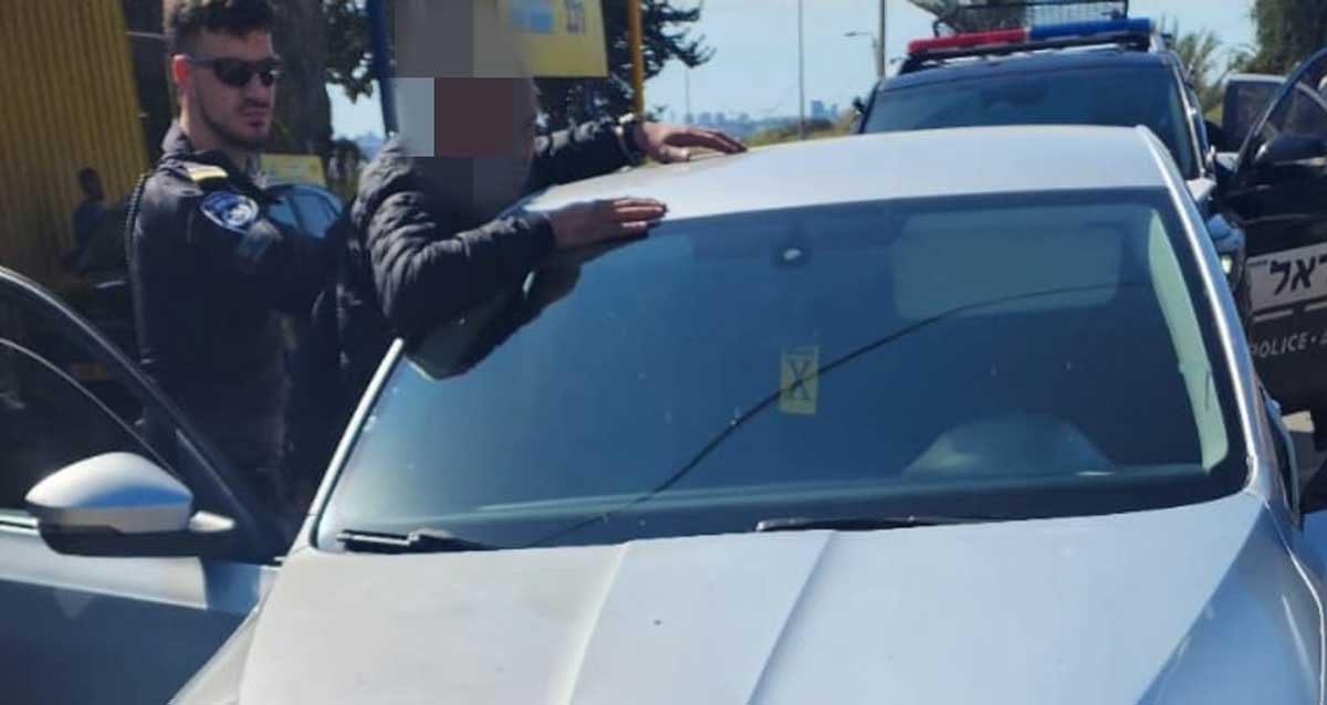 שוטר עוצר חשוד. הפנים של החשוד מטושטשות. החשוד נשען על רכב עם ידים על גג הרכב