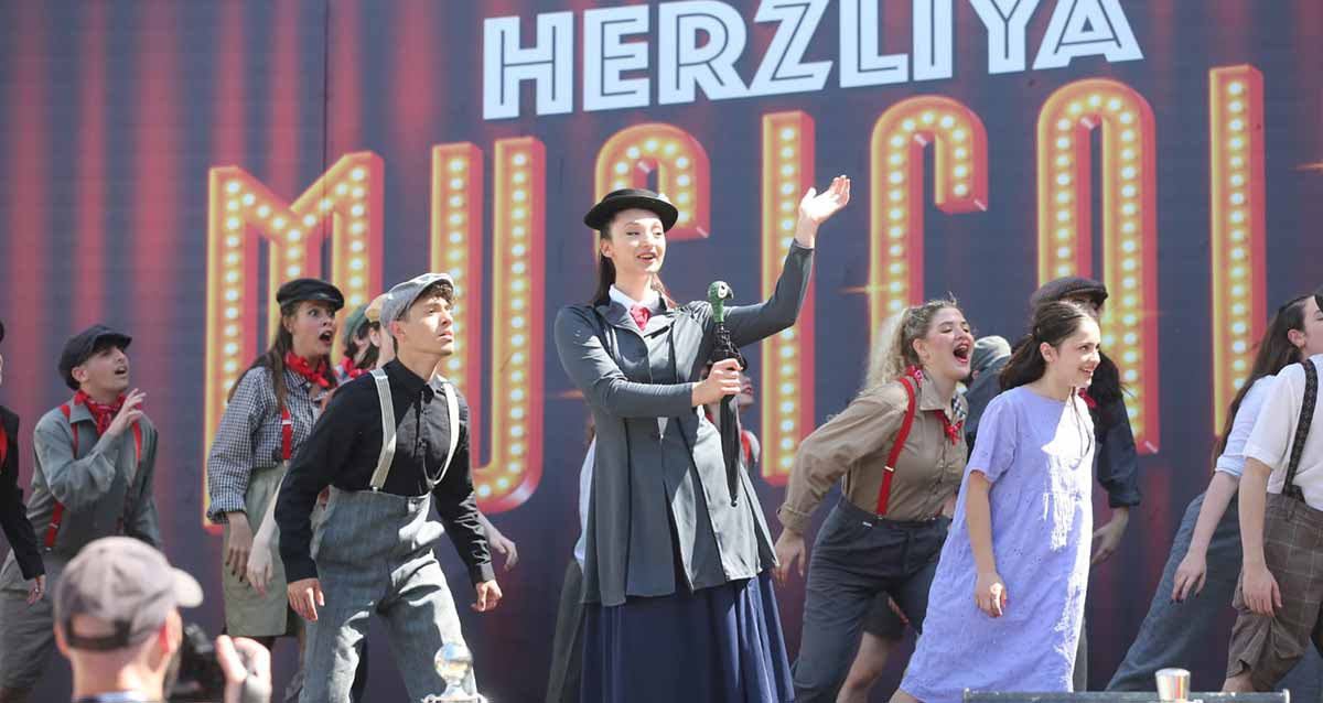 אירוע פורים המרכזי בהרצליה. להקה על הבמה. מאחוריהם רקע עם כיתוב באנגלית: HERZLIYA MUSICAL