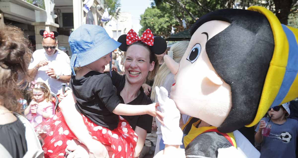 אירוע פורים המרכזי בהרצליה. אישה מחופשת עם ילד על הידיים מול איש מחופש לליצן.