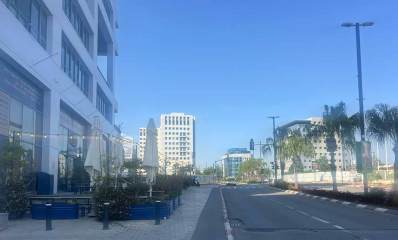אזור התעשייה רעננה. בצד שמאל מבנה בן ארבע קומות. בית קפה בקומת הקרקע ואזור ישיבה עם שמשמיות במדרכה הרחבה. ברקע מבנים גבוהים.
