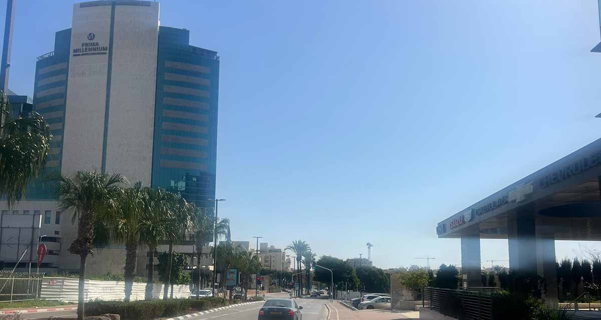 מלון פרימה מילניום באזור התעשייה רעננה בצד שמאל של התמונה. בניין גבוה עם חלק אמצעי בצבע לבן ללא חלונות.