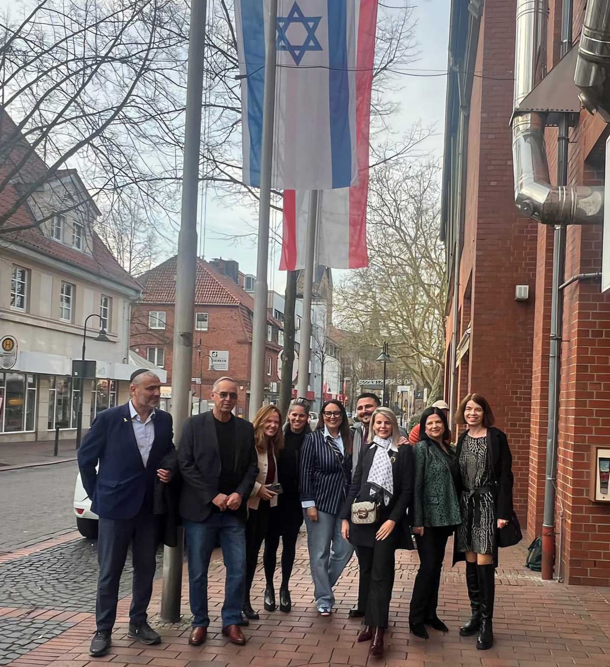 המשלחת מרמת השרון בעיר הגרמנית התאומה בתמונה קבוצתית במדרכה. מעליהם דגל ישראל ודגל שאחריו מוסתר