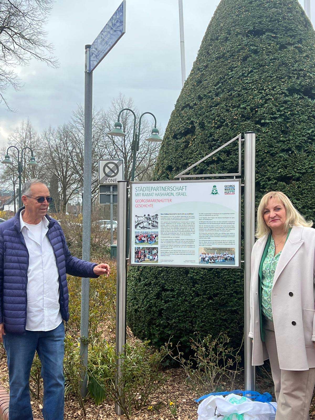 ראשי הערים של רמת השרון והעיר התאומה בגרמניה עומדים משני הצדדים של שלט שהוצב לציון הקשרים. השלט בגרמנית וכולל גם ארבע תמונות.
