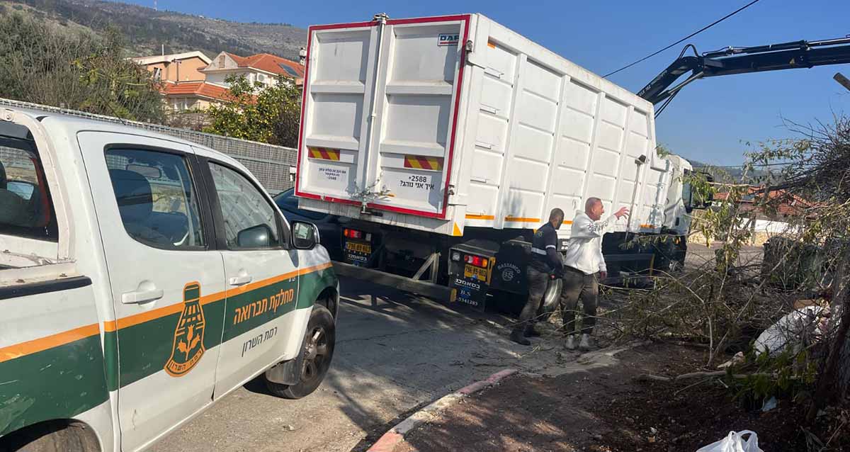 עובדי עיריית רמת השרון בקריית שמונה. משאית איסוף פסולת וטנדר של מחקת התברואה בעיריית רמת השרון, אוספים אשפה. שני עובדים עומדים ליד המשאית.