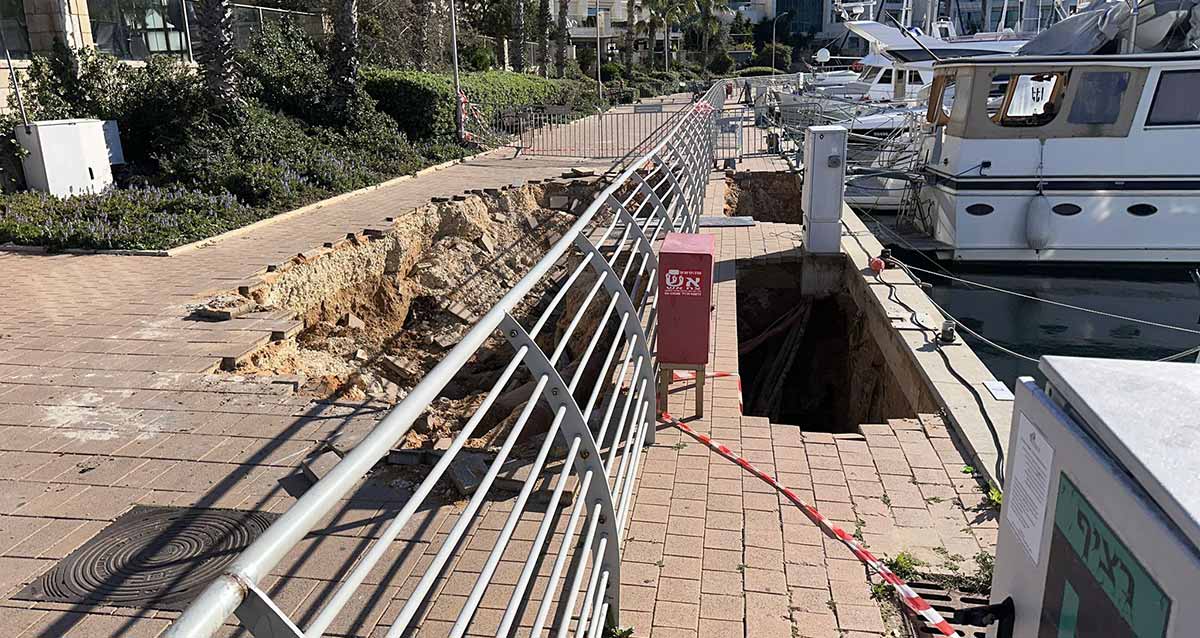 בולען במספנת מרינה הרצליה. בור עמוק ברציף. בצד שמאל ארון כיבוי אש בצבע אדום, ומאחוריו מעקה מתכת, ואחרי המעקה בור במדרכה. בצד ימין סםינות.