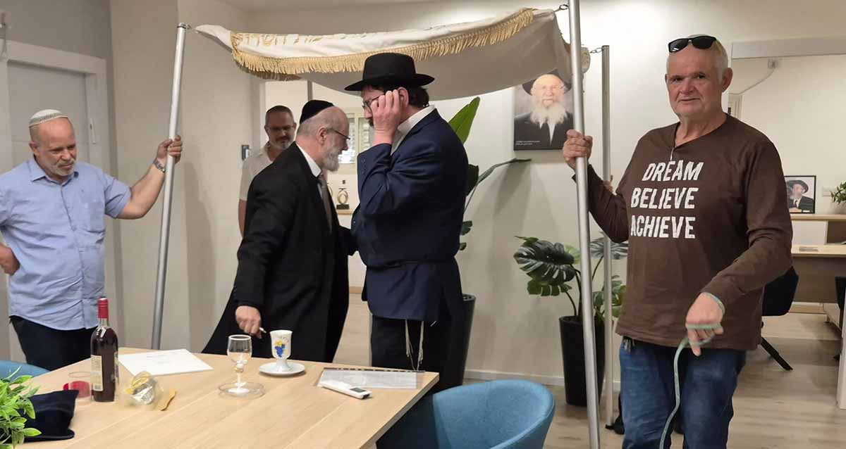 חתונה במועצה הדתית רמת השרון. אנשים אוחזים בעמודי החופה. מתחת לחופה שני אנשים דתיים.