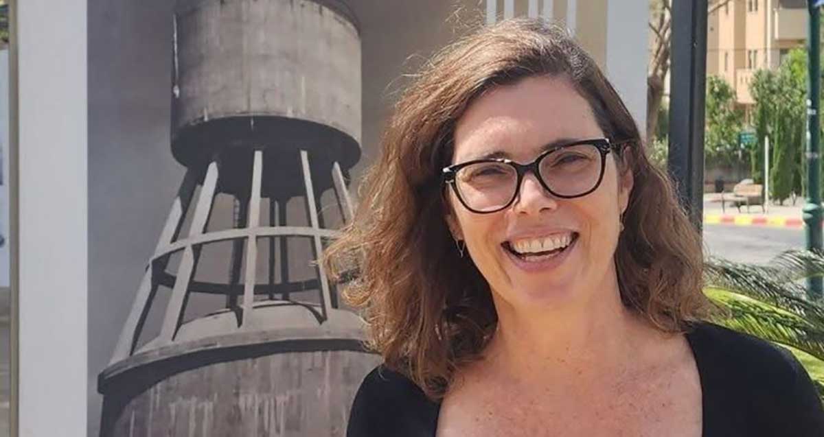 אדריכלית העיר רמת השרון אורית בן אסא על רקע תמונה של מגדל מים על קיר.