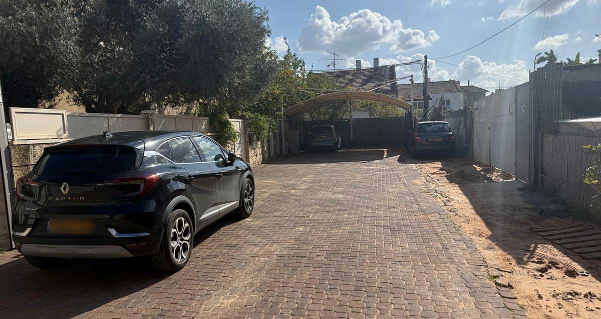 הסככה ברחוב צדיקי לוז בכפר סבא, סככה עם גג מעוגל לחנייה של שני כלי רכב. רכב אחד בתוך הסככה. רכב אחד מימין לסככה.
