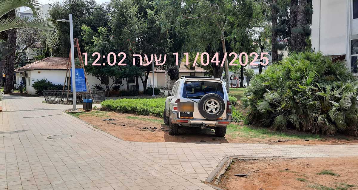 ג׳יפ כסוף מחנה בגינה. על התמונה מותבע התאריך 11/04/2025 שעה 12:02. ברקע מבני העירייה
