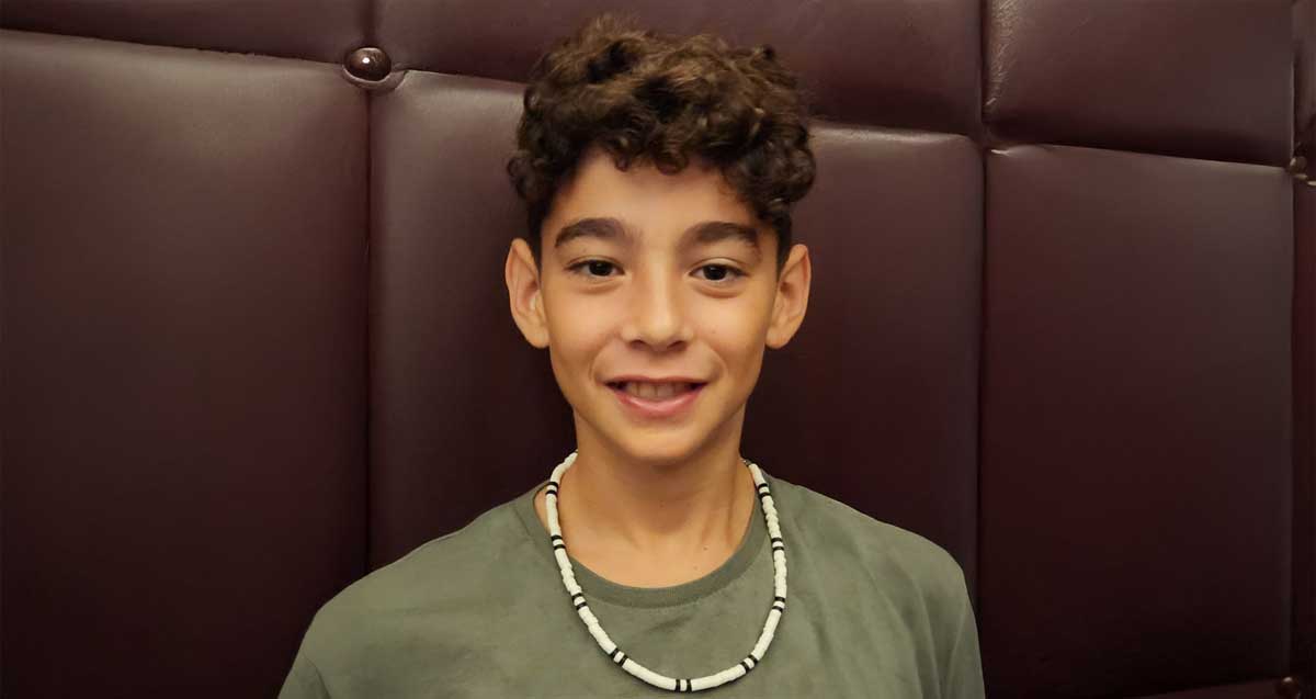 רום וילדר ז"ל, בחולצה ירוקה ושרשרת לבנה עם פסים שחורים סביב צווארו.