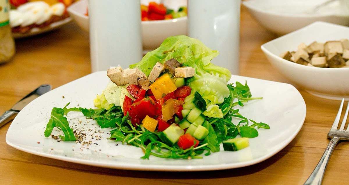 סלט טופו וירקות על מצע של עלים ירוקים, בצלחת לבנה.