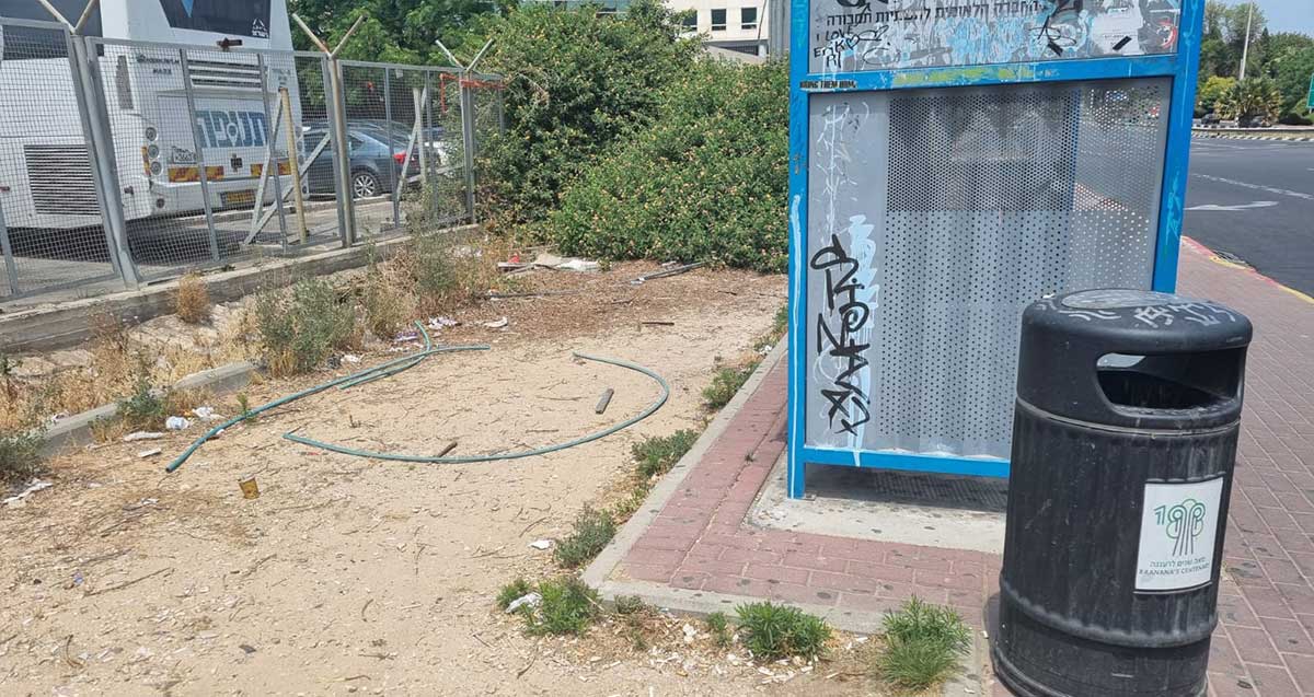 תחנת האוטובוס בדרך השרון. גרפיטי על דופן התחנה. פח אשפה שחור ליד התחנה. מאחורי התחנה זרוקים צינורות פלסטיק ואשפה.