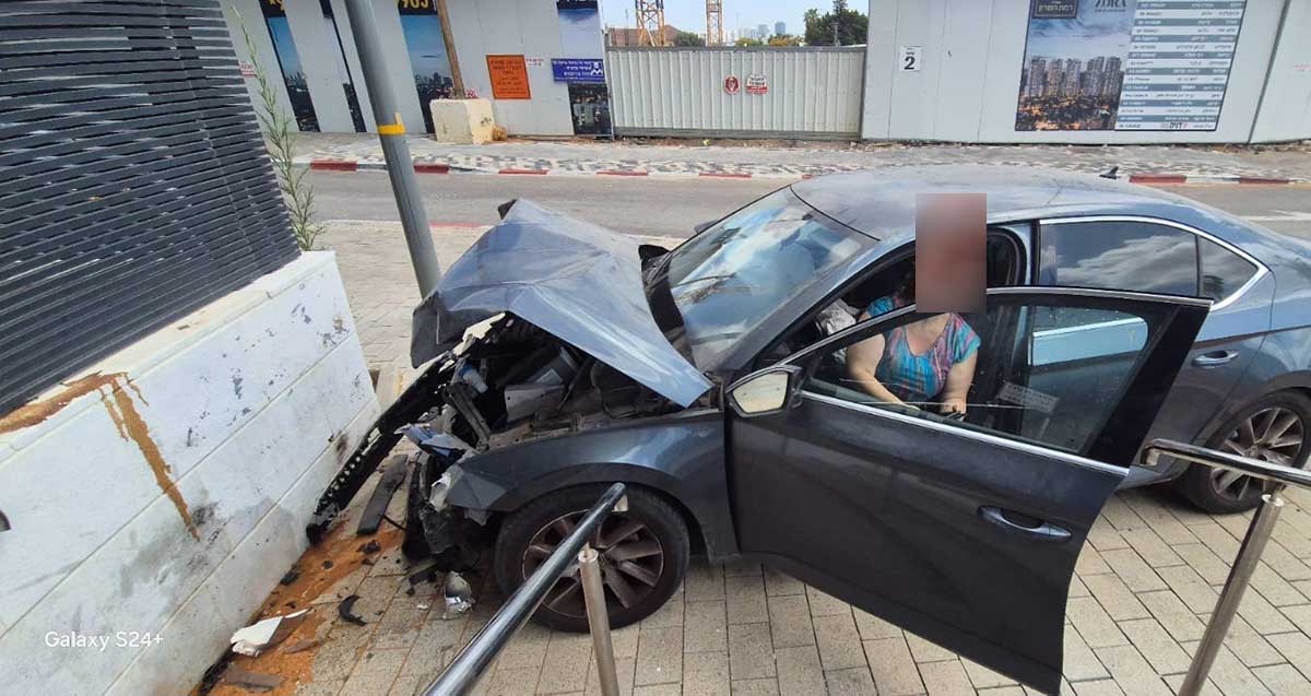 רכב התנגש במגדלי אאורה ברמת השרון. הנהגת יושבת ברכב כאשר דלת הנהגת פתוחה. חזית הרכב מרוסקת ומכסה המנוע מורם.