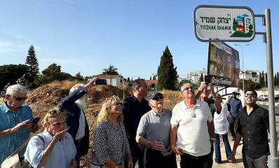 חיים ברודיא ואנשים נוספים סביבו מתבוננים בשלט רחוב יצחק שמיר