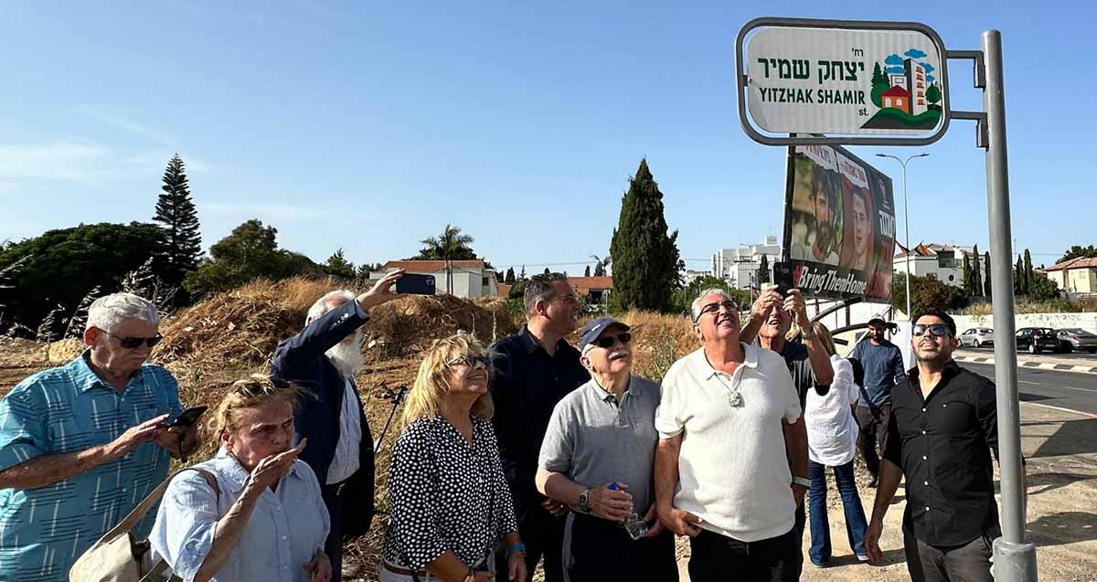 חיים ברודיא ואנשים נוספים סביבו מתבוננים בשלט רחוב יצחק שמיר