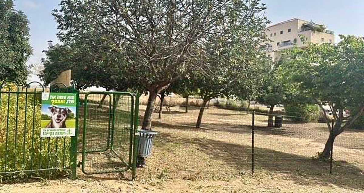 גינת הכלבים הזמנית בחורשת החקלאים בשכונת נווה זמר. גינה של חול עם עצים. בכניסה שלט עם תמונה של ראש כלב וכיתוב: הוא עשה את שלו, ואתם? רעננה נקייה
