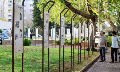 תערוכת "עד האיחוד" בפארק. שורה של שלטים ארוכים וגבוהים, עם כותרת בכיתוב: עד האיחוד, ובכל שלט שלוש או ארבע תמונות. שני אנשים בשביל של הפארק עומדים וצופים באחד השלטים.